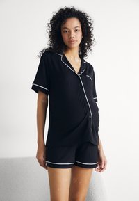Svart graviditet pysj-sett med kortermet knapp-up topp med lomme og matchende shorts, detaljert med hvit trim. Myk, elastisk fabric.