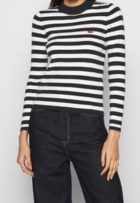 Pull côtelé noir et blanc à rayures, doté d'un col rond et d'un petit logo rouge Levi's sur la poitrine, associé à un jean foncé.