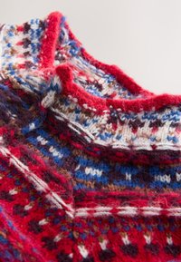 Gebreide trui met een hoge kraag, met een meerkleurig patroon in rood, blauw, bruin en wit. Getextureerd wollen materiaal met levendige tinten.