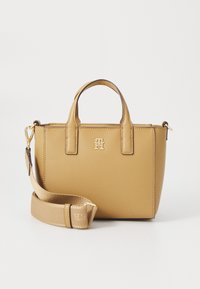 Sac à main en cuir tan avec deux poignées supérieures et une bandoulière amovible. Présente un logo doré à l'avant et un design structuré. Fini texturé.