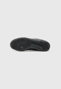 Svart sneakersole med teksturert gummi, med et særegent mønster og preget merkevare. Flat, strømlinjeformet form for stabilitet.