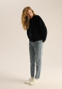 Czarny prążkowany kardigan z złotymi guzikami, noszony na jasnoniebieskich dżinsach prostych i białych sportowych trampkach. Miękka, teksturowana dzianina.