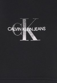 Felpa nera con logo "CALVIN KLEIN JEANS" in argento. Il tessuto è liscio con una superficie leggermente strutturata. Design semplice e moderno.
