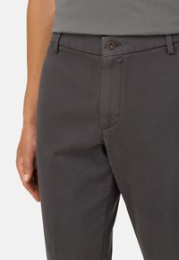 Donkergrijze broek van textuurstof, met een voorzak, subtiele stiksels en een bruine knoopsluiting.