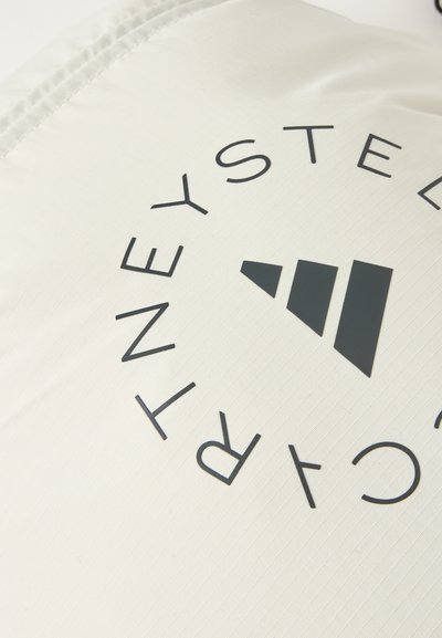 Μαύρο γεωμετρικό λογότυπο με τη λέξη "STELLA McCARTNEY" σε κυκλική διάταξη πάνω σε ελαφρώς έγχρωμο υφασμάτινο υλικό με υφή.