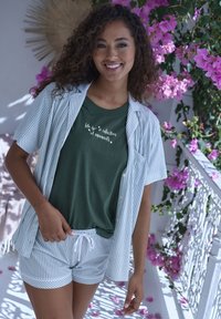 Groen T-shirt met witte tekst, gestreepte kortemouwen shirt en bijpassende gestreepte shorts. Bloemrijke achtergrond met roze bloemen.