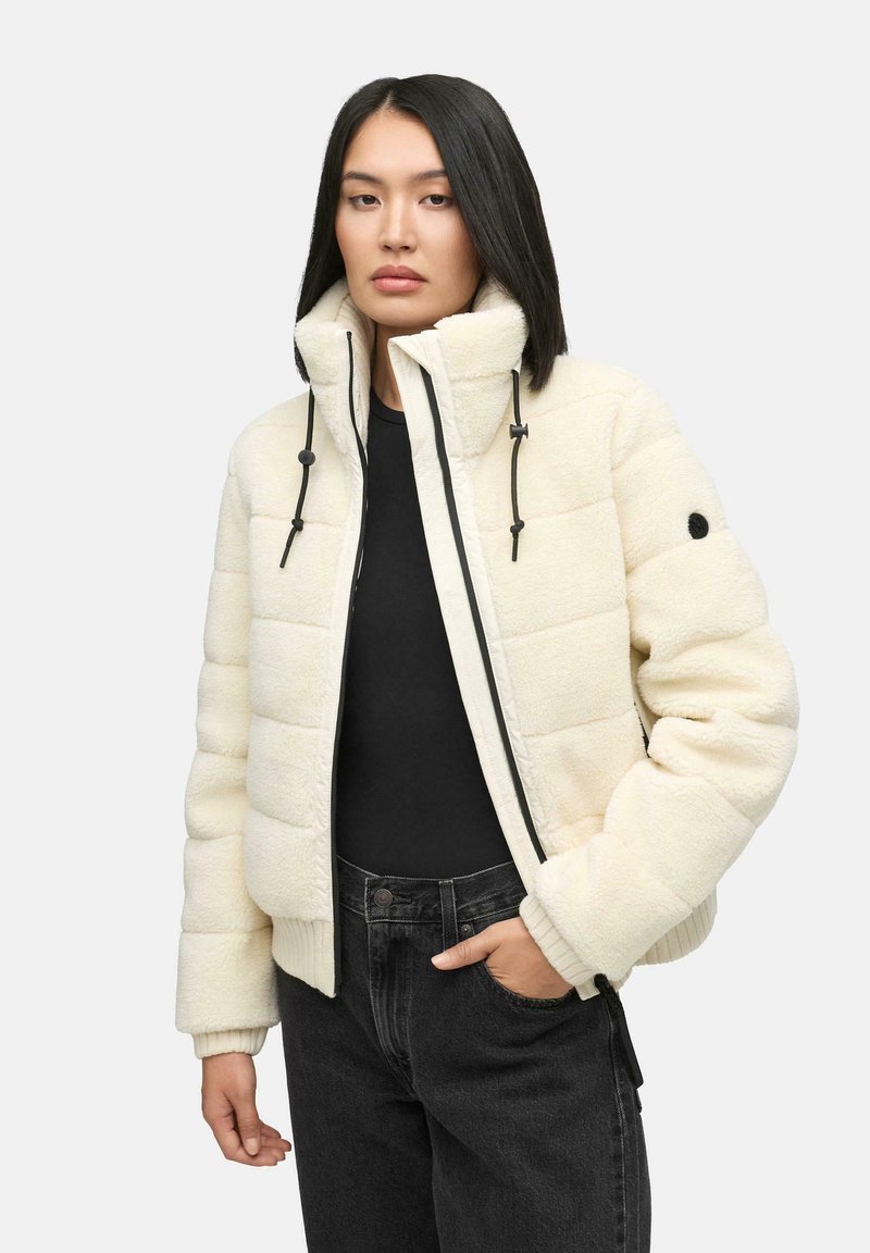 Witte fleece pufferjas met hoge kraag, verstelbare trekkoorden, ribgebreide manchetten en ritsluiting, gecombineerd met zwarte jeans.