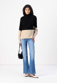 Un pull col roulé noir et beige à manches longues, associé à un jean flare bleu clair et des ballerines beiges, portant un sac à main noir.
