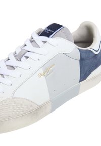 Sneaker bianca con una combinazione di pelle liscia, suede grigio e texture in rete. La finitura è completata da elementi dorati e un design a punta arrotondata.