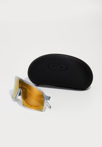 Óculos de sol com armação transparente e lentes amarelas espelhadas, acompanhados de um estojo rígido preto de proteção com um logo.