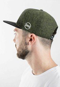 Green herringbone cap with a black flat brim. Features a white logo on the side and textured fabric, showcasing a structured design.