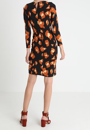 Robe noire avec motif abstrait orange, manches longues, détail dos en trou de serrure, forme ajustée, associée à des sandales à talons blocs strappées marron.