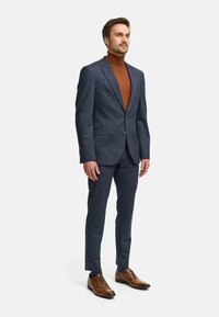 Marineblauw, gestructureerd pak met twee knopen en notch revers, gecombineerd met een bruine coltrui en bruine leren schoenen.