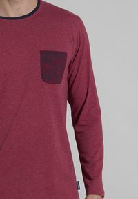 Langsleeve overhemd in bordeauxkleurige katoenmix met een marineblauwe halslijn en een gebloemde bordeauxkleurige zak. Soepele textuur, ontspannen pasvorm.