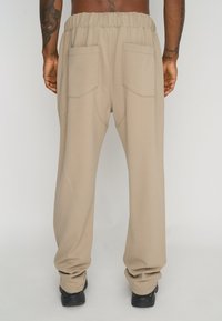 Beige sweatpants with a drawstring waistband, featuring two back pockets and a relaxed fit. The fabric has a smooth texture and subtle stretch.