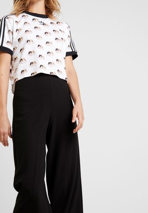 Cropped white t-shirt with a playful pattern of small dog illustrations. Black accents on sleeves. Paired with loose black pants.