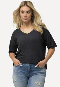 Černé tričko s véčkovým výstřihem vyrobené z měkkého materiálu, s krátkým rukávem, spárované s opranými světle modrými džíny. Jednoduchý design s volným střihem.