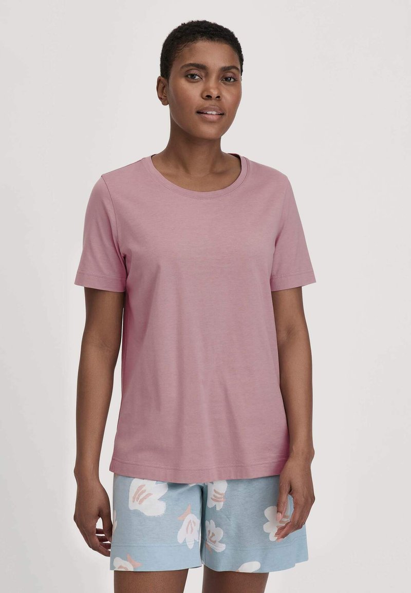 Kurze rosa T-Shirt mit Rundhalsausschnitt, kombiniert mit hellblauen Shorts, die ein weißes Blumenmuster aufweisen.