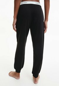 Svarta loungebyxor med elastiska ärmslut och midjeband. Calvin Klein-logotyp på midjebandet. Mjukt tyg med avslappnad passform.