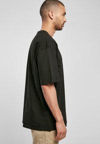 Black cotton t-shirt with short sleeves, loose fit, round neckline, and a straight hem, displayed on a model viewed from the side.