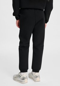 Zwarte sweatpants met een elastische tailleband en boorden, zachte textuur, taps toelopend ontwerp. Draagt met zilveren sneakers en witte sokken.