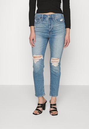 Jeans de lavagem azul claro, desfiados, com rasgos frontais, cintura alta e design de perna reta. Combinados com sandálias pretas de salto alto com tiras cruzadas.