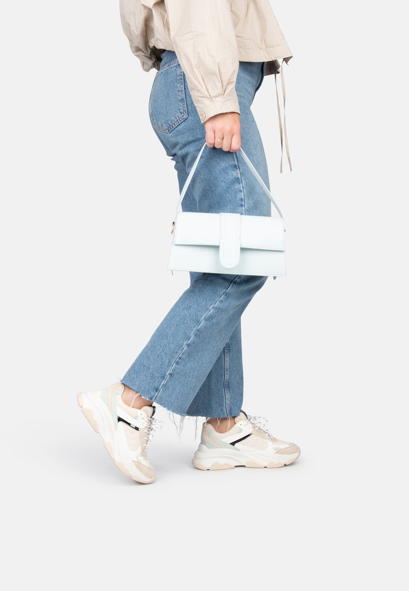 Borsa azzurro chiaro con manico superiore, forma rettangolare, finitura liscia e chiusura con patta. Abbinata a jeans di jeans blu e sneakers bianche.