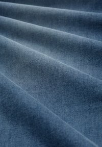 Tissu en denim bleu doux avec des plis diagonaux et une texture de tissage visible.