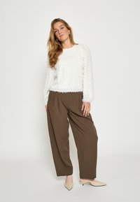 Valkoinen teksturoitu neule, jossa siksak-kuvio, yhdistettynä löysiin ruskeisiin housuihin. Asu sisältää neutraalin sävyiset teräväkärkiset ballerinat. Yksinkertainen muotoilu.