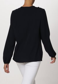 Námořnická modrá halenka s dlouhým rukávem a kulatým výstřihem, vyrobená z měkké látky, s volným střihem a elastickými manžetami. Jednoduchý, nezdobený design.