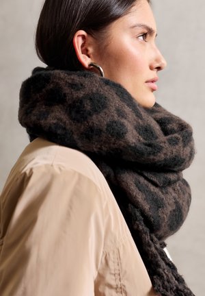 Brown and black spotted scarf made of soft, textured fabric, draped loosely around the neck, paired with a light beige coat.