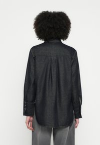 Σκούρο τζιν πουκάμισο με μυτερό γιακά, μανσέτες με κουμπιά και άνετη εφαρμογή. Διαθέτει πιέτα στην πλάτη και ραφές με αντίθετο χρώμα.