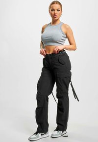 Svarta cargo-byxor med flera fickor, justerbar midja och dragsnören, kombinerat med en grå cropped topp och sportiga sneakers.
