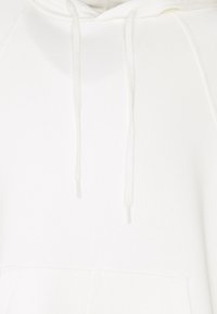 Bílá mikina s kapucí vyrobená z měkkého materiálu, vybavená šňůrkou na stažení, přední klokankovou kapsou a žebrovanými manžetami a spodním lemem. Bez vzorů nebo akcentů.