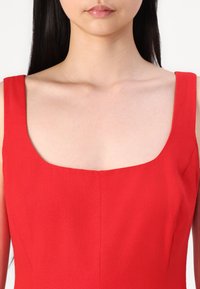 Robe sans manches rouge avec un décolleté carré, texture lisse et coupe ajustée. Pas de motifs ou d'ornements visibles.