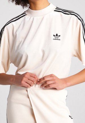 Chemisier à col montant crème Adidas avec des accents noirs à trois bandes sur les manches et un petit logo sur la poitrine. Tissu doux, coupe décontractée.