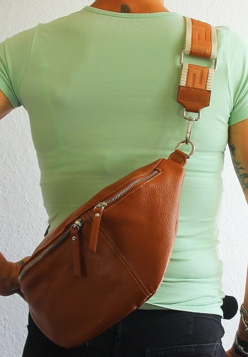 Sac en cuir brun en bandoulière avec deux poches zippées, présentant une surface texturée et une sangle réglable à motif.