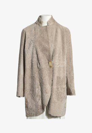 Abrigo largo beige de shearling con dos bolsillos delanteros y un único cierre con broche dorado en el cuello, mostrado en un maniquí blanco.