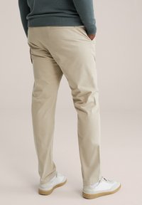 Pantalon en coton beige à coupe décontractée avec poches latérales, associé à des baskets blanches à semelle marron clair. Pull texturé bleu clair.