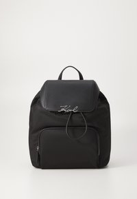 Mochila de nylon negra con una solapa de piel, marca plateada en la parte delantera y un bolsillo con cremallera en la parte frontal. Diseño sencillo con un asa en la parte superior.