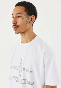 Witte oversized t-shirt van katoen, met een zwart stippenpatroon op de voor- en achterkant. Zachte textuur, ronde halslijn.