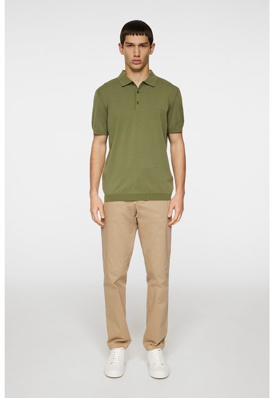 Chemise polo vert olive à manches courtes, avec une patte de boutonnage à trois boutons, associée avec un pantalon chino beige et des baskets blanches. Design simple et ajusté.