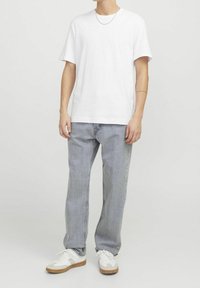 Camiseta de algodón blanca con un corte holgado, combinada con jeans rectos en un tono gris claro y zapatillas blancas con acentos en beige.