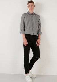 Grå knap-op skjorte med rullede ærmer, parret med sorte tapered bukser og hvide sneakers. Stoffet ser glat ud med en subtil tekstur.