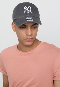 Gorra de béisbol gris con logo blanco bordado en la parte frontal, correa ajustable, usada con una camiseta rosa clara.