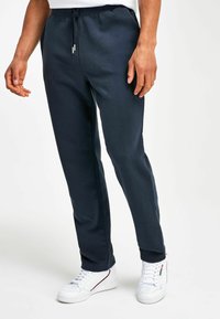 Pantalones de chándal azul marino hechos de material suave, con una cintura elástica y cordón, y bolsillos laterales, combinados con zapatillas blancas.