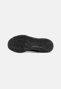 Sort sneakersål med tekstureret gummimønster, der har forskellige dækdesigns og Under Armour-logoet prentet på siden.