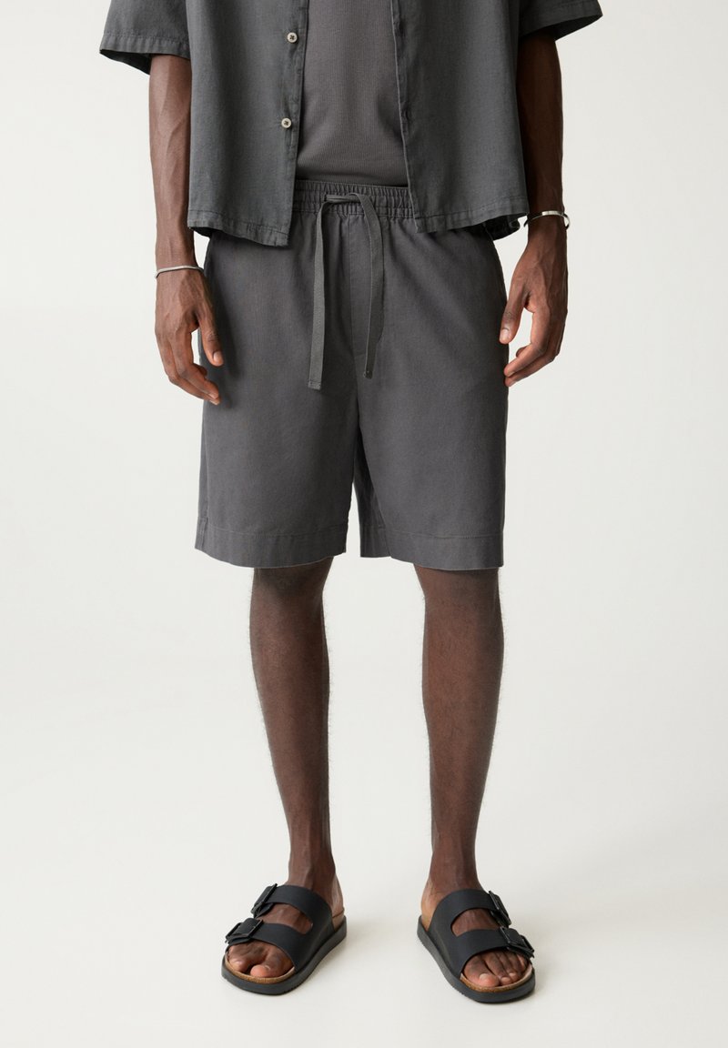 Grå, løstsiddende skjorte og shorts lavet af letvægtsstof, med elastisk talje og flade sandaler med to spændeaccenter.