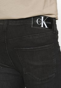 Svarta jeans i denim med en subtil textur, som har en distinkt bakficka och en rektangul är svart etikett med "Calvin Klein Jeans" i vitt.
