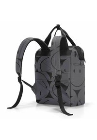 Mochila de tela gris con un patrón abstracto negro. Presenta correas dobles y un asa en la parte superior. Cierre de cremallera y bolsillos laterales visibles.